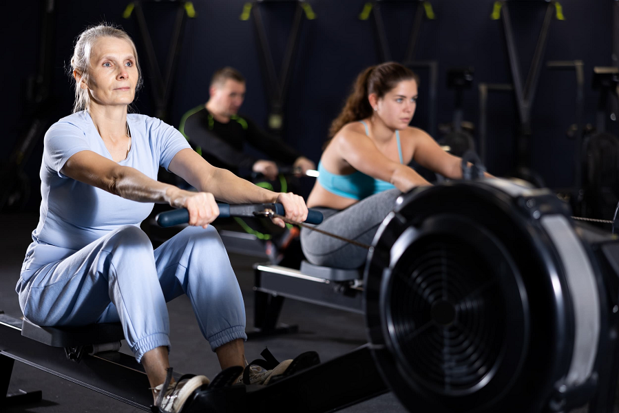 A group of adults use rowing machines in a group fitness class